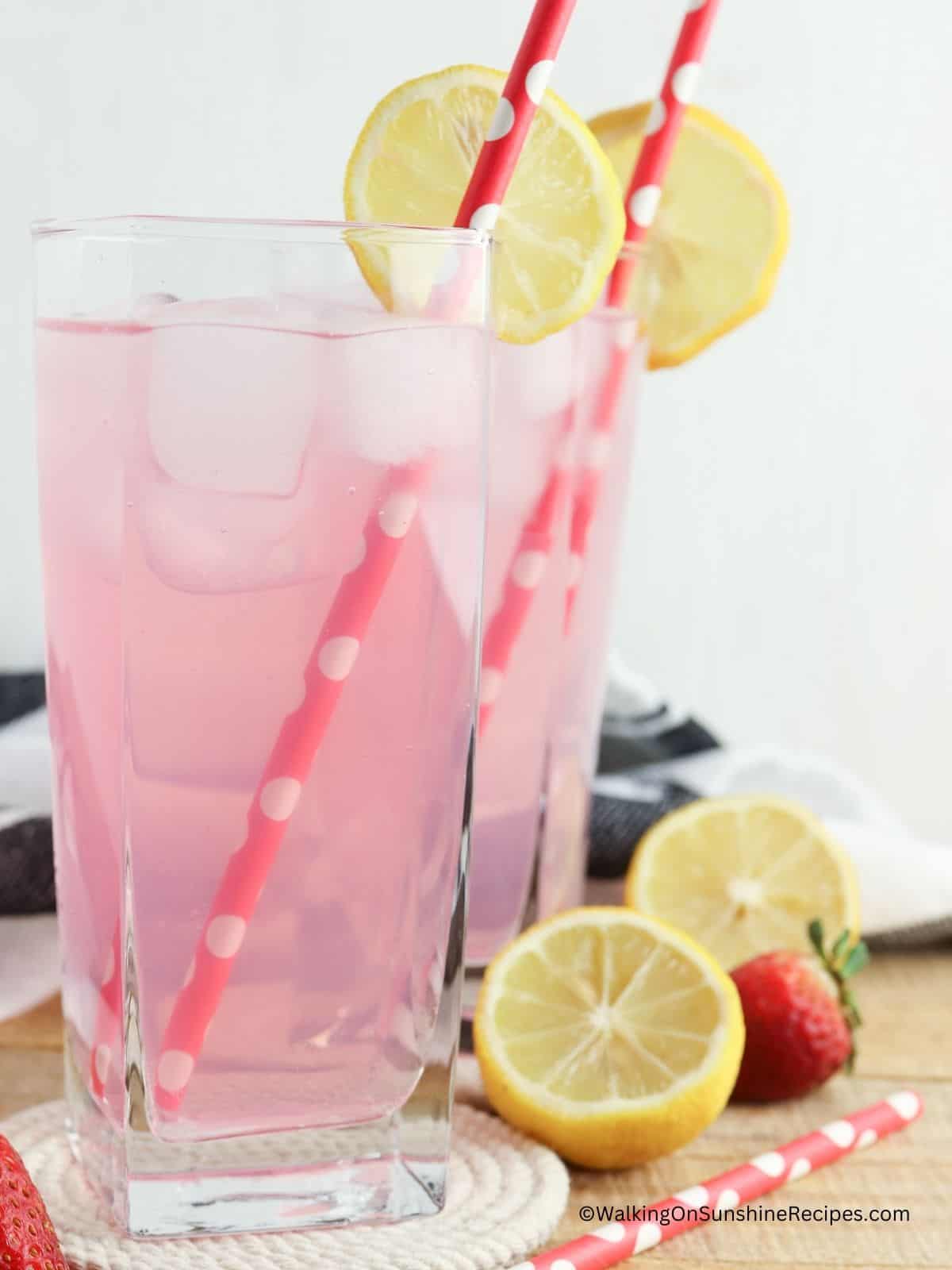2 glasses of strawberry beverage with sliced lemons, strawberries and straws.