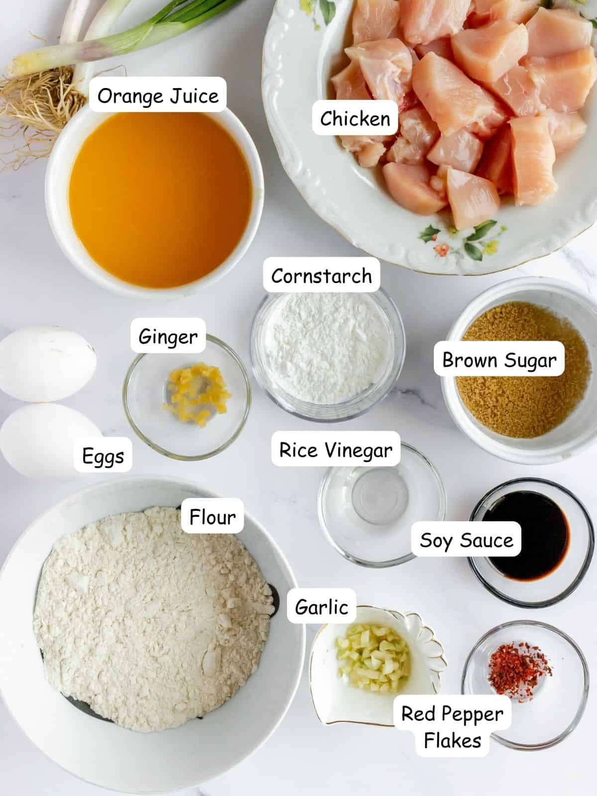 Ingredients in bowls, chicken, flour, garlic, eggs, red pepper flakes, orange juice, brown sugar, ginger, rice vinegar, cornstarch.
