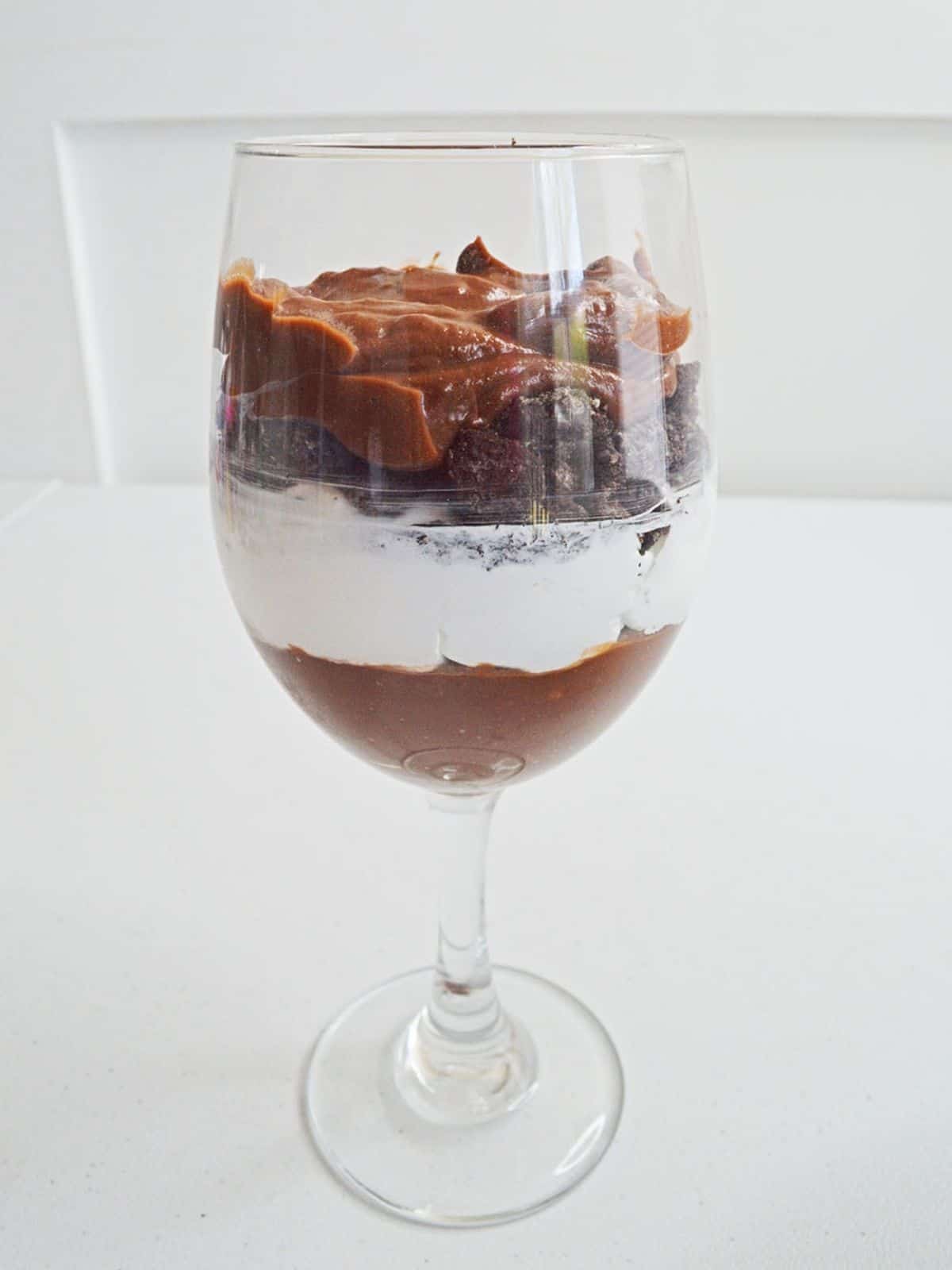 Layer chocolate pudding, whipped cream with crushed cookies in glass.