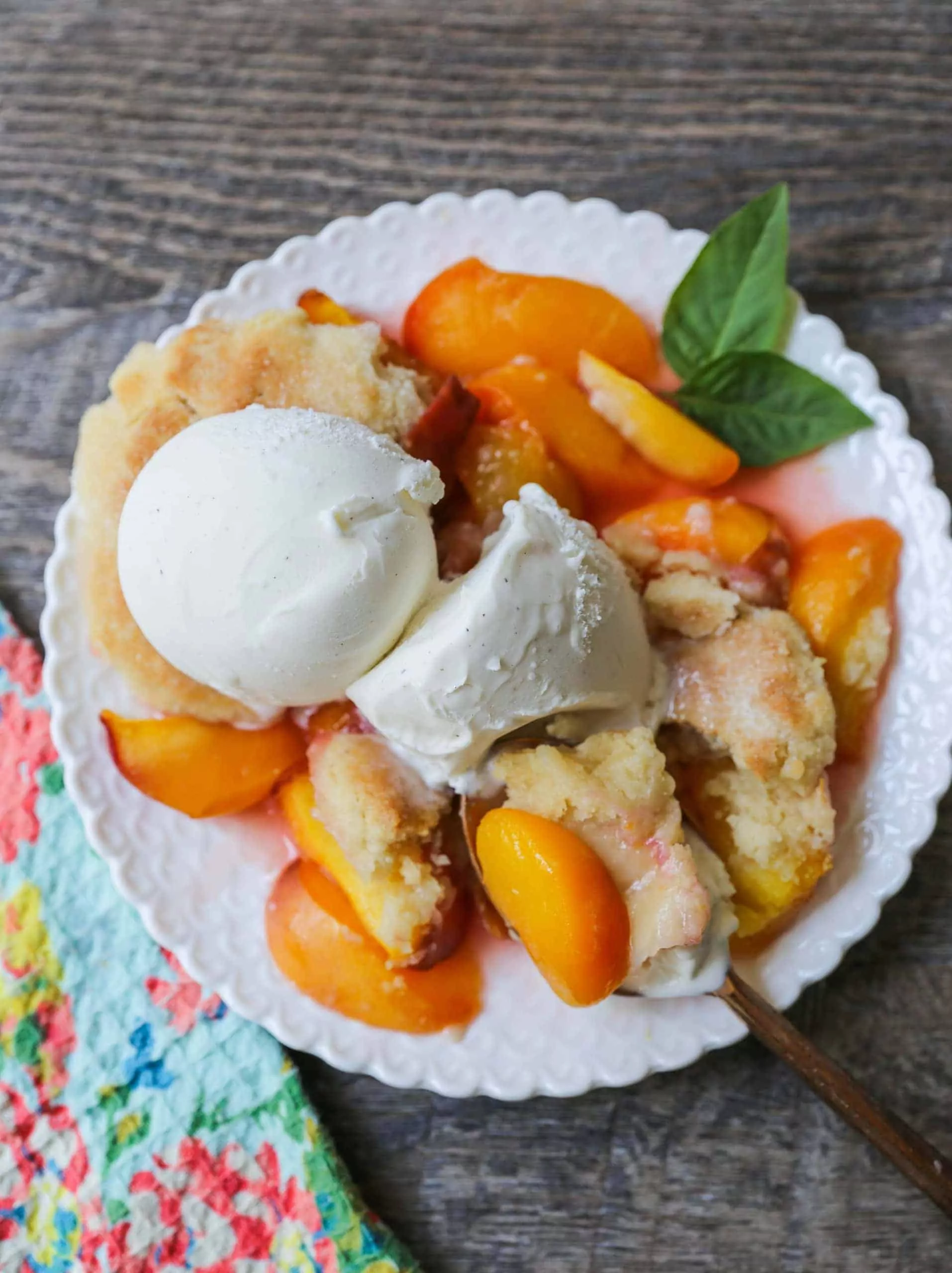 peach cobbler with ice cream on white plate with spoon.