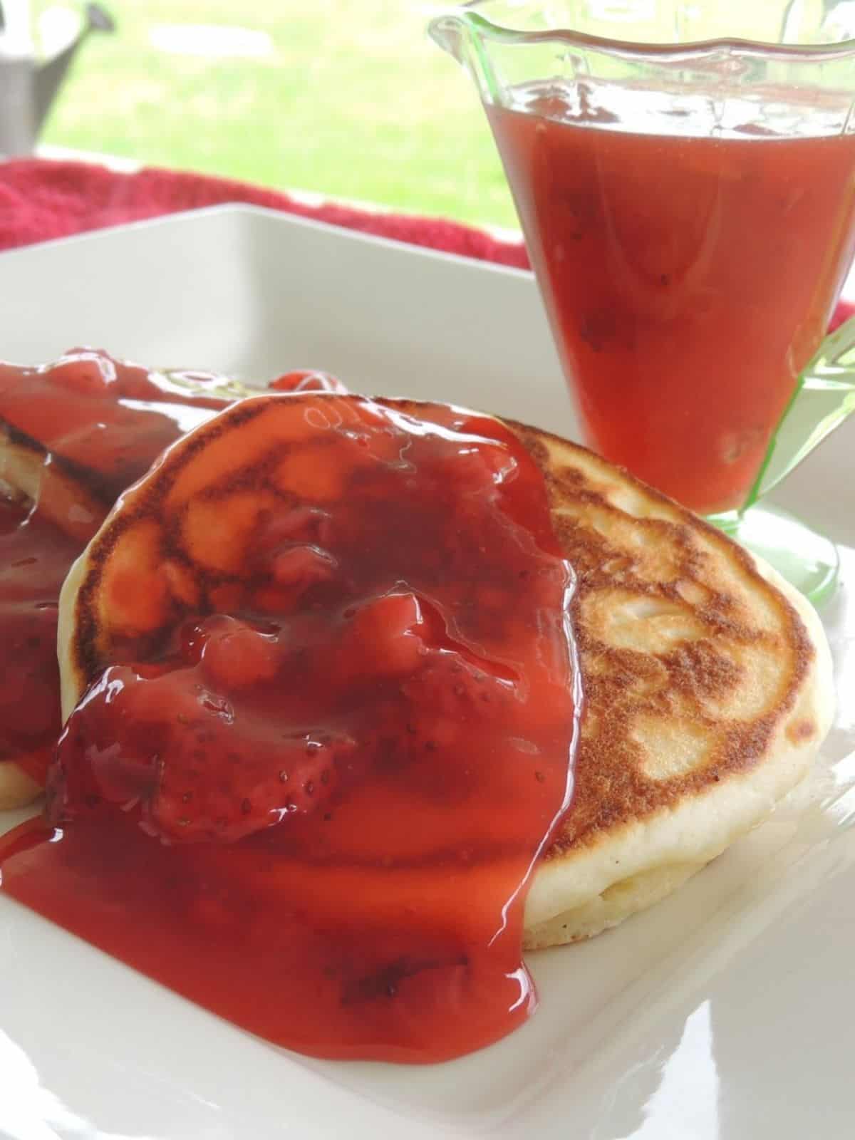 pancakes on plate with strawberry sauce on top.