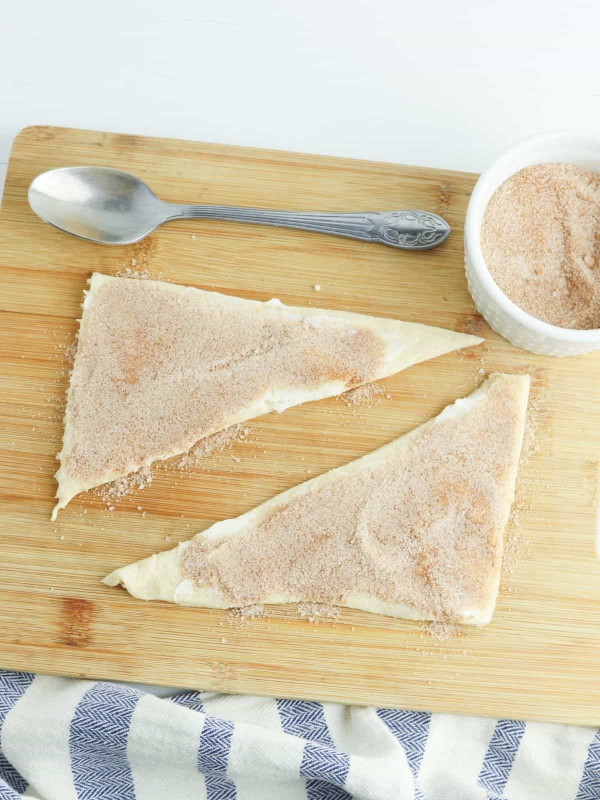 cinnamon and sugar spread on top of crescent roll triangles on top of cutting board.
