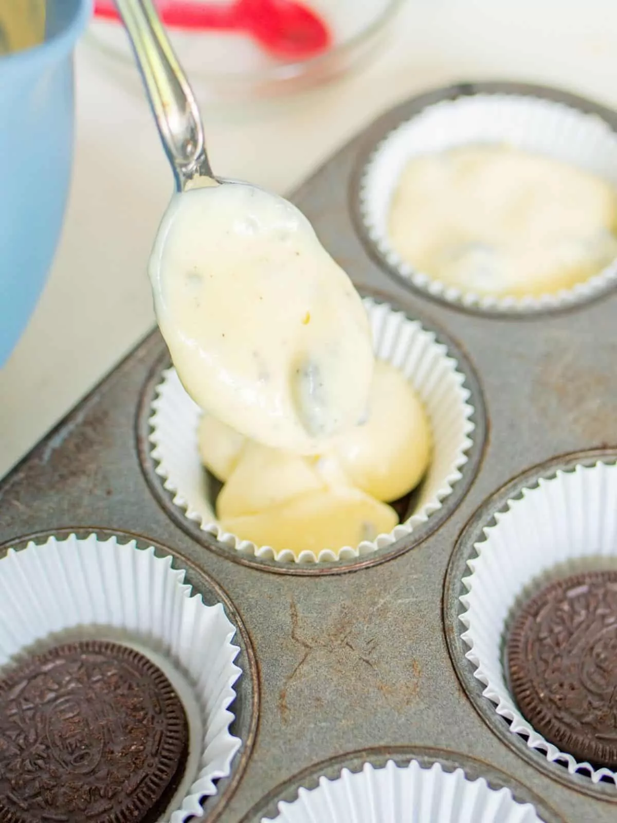 Adding cheesecake mixture to cupcake pan with Oreo cookies in the bottom of each cupcake liner.