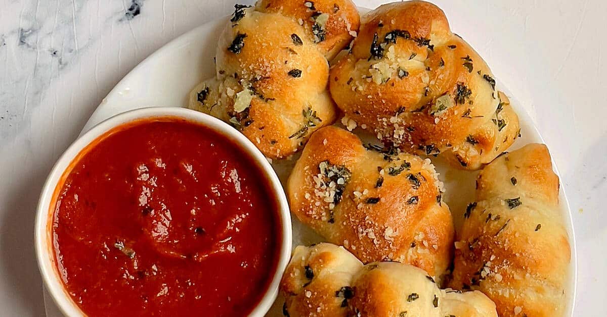 garlic knots on plate with marinara sauce in bowl.