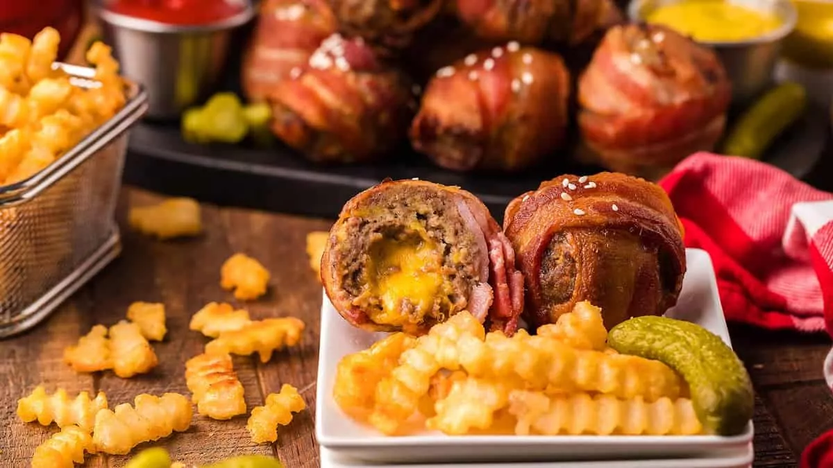 cheeseburger bites wrapped in bacon with French fries and pickles.