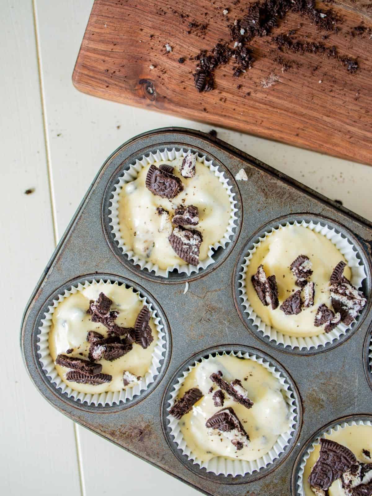 mini cheesecakes with cookie crumbs in muffin pan before baking.