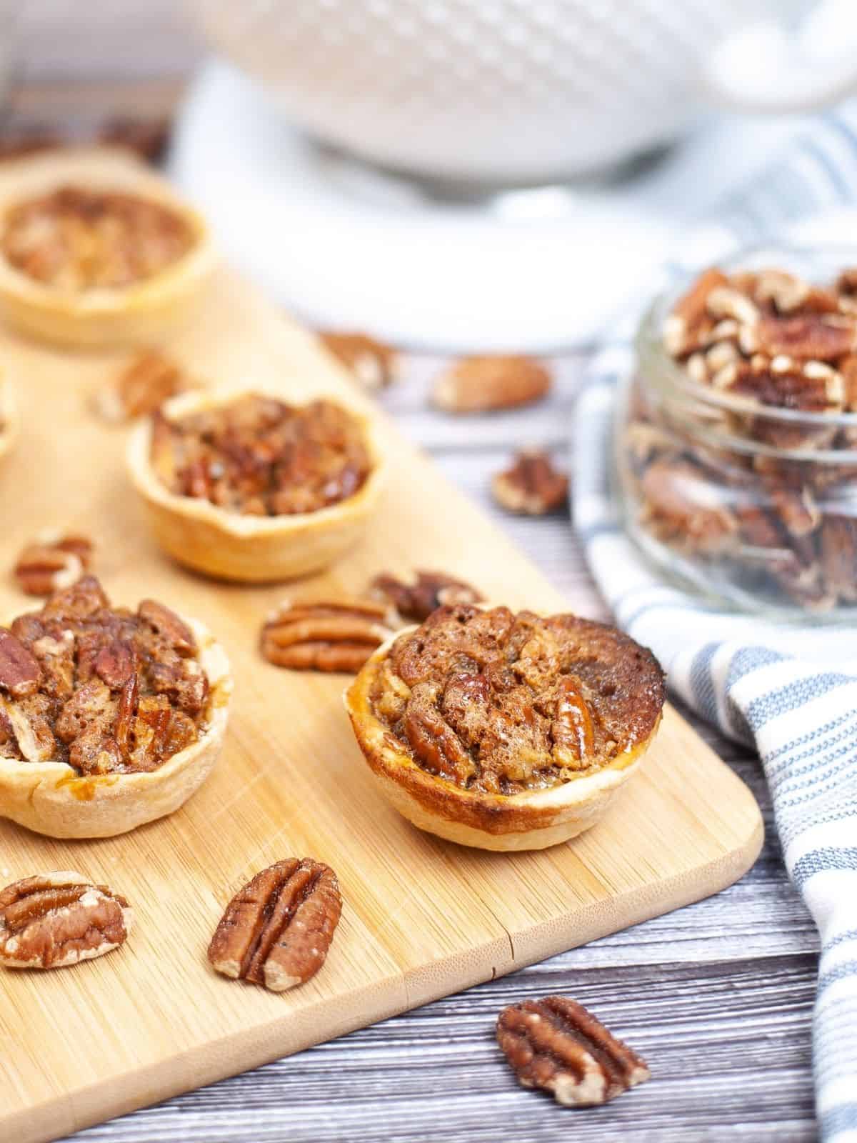 Mini pie tartlets with pecans on cutting board.