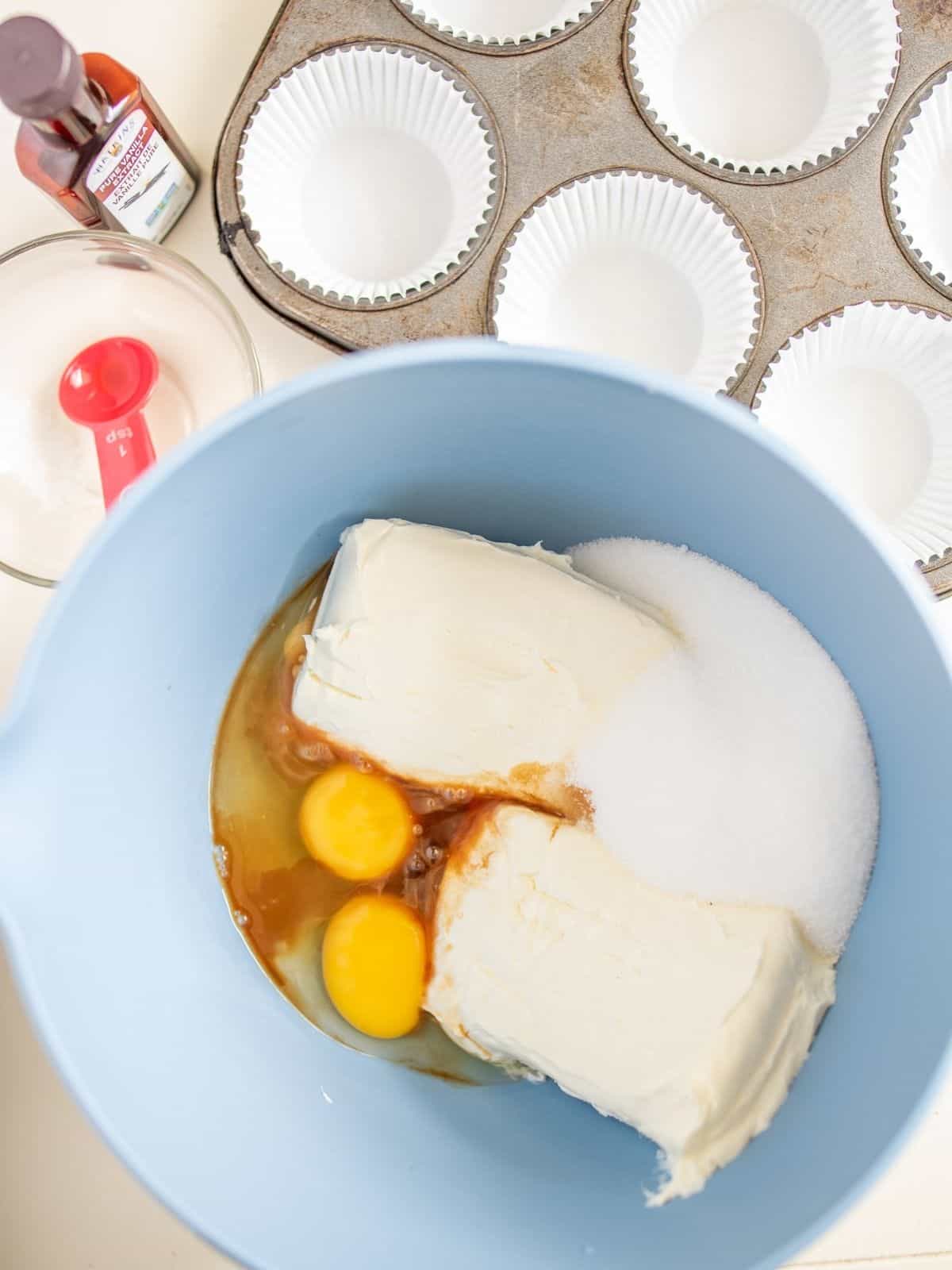 cream cheese, eggs and vanilla extract in blue mixing bowl.