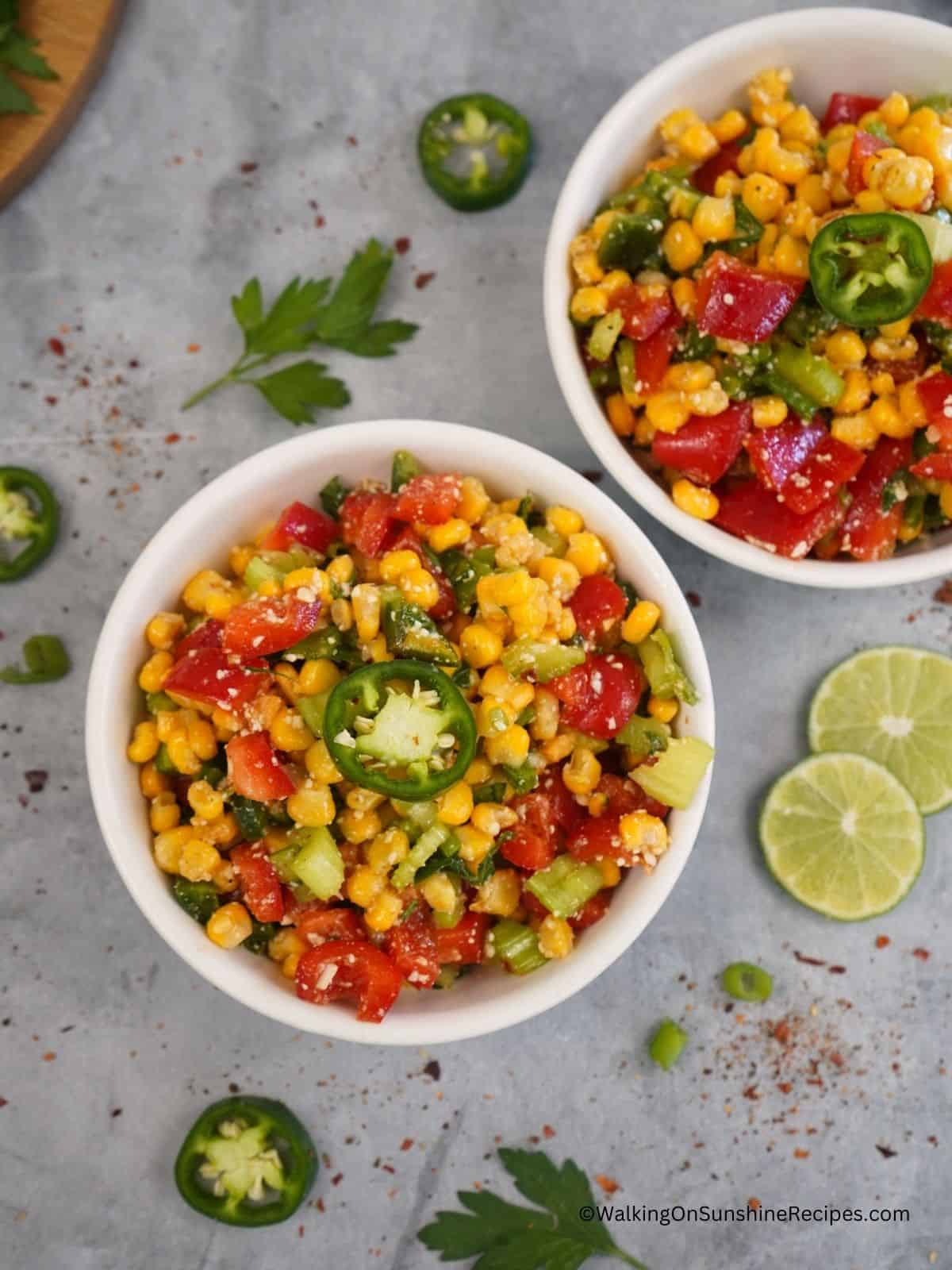 2 bowls of salad with corn, tomatoes, peppers and more.