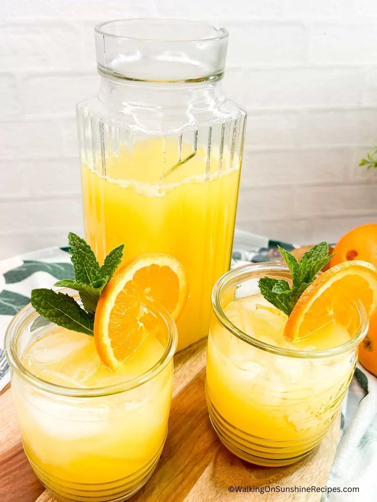 pineapple punch served in two glasses with sprig of mint and orange slices.