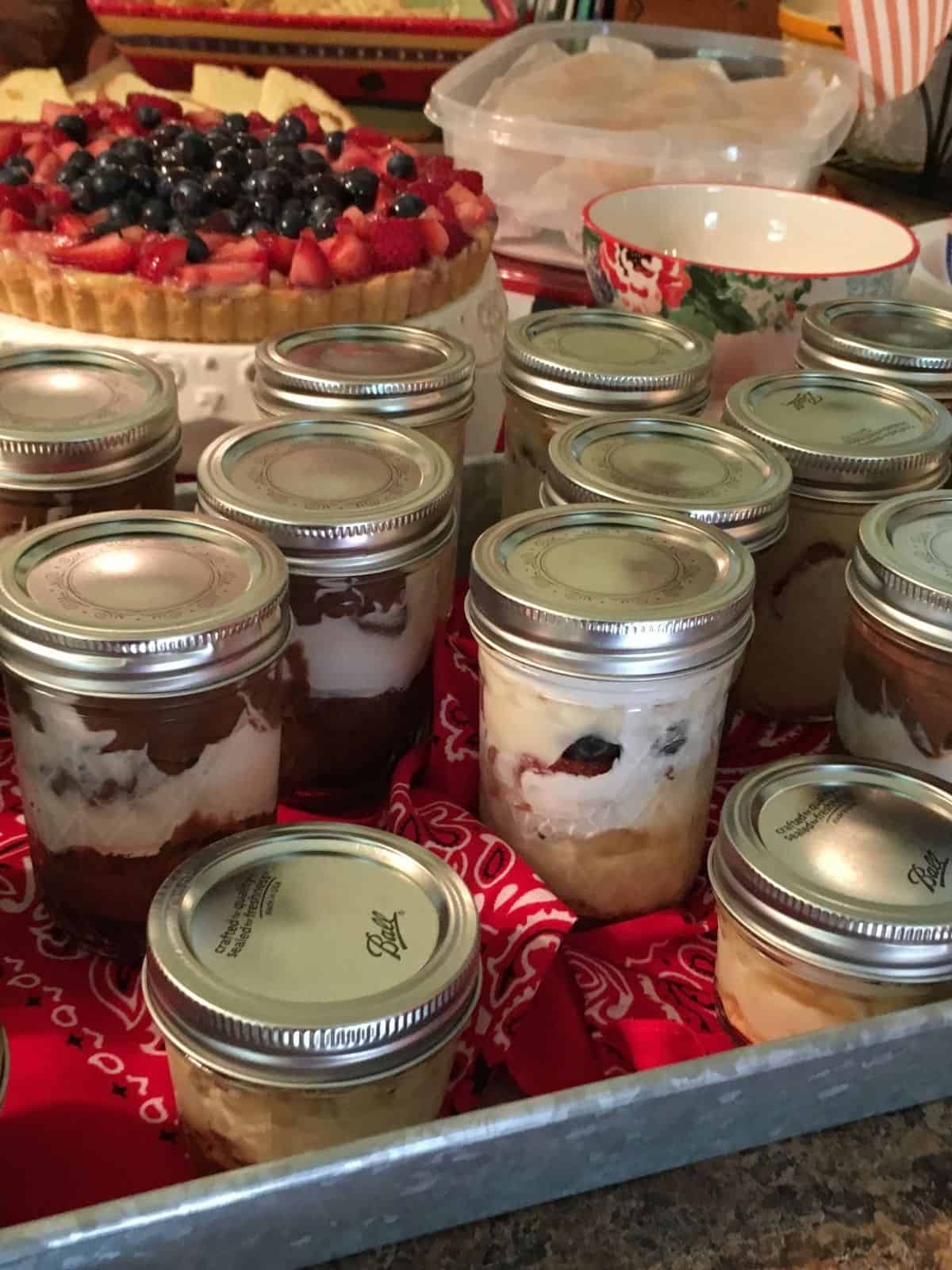 mason jars filled with pudding, cookies and fruit on tray with fruit tart in background.