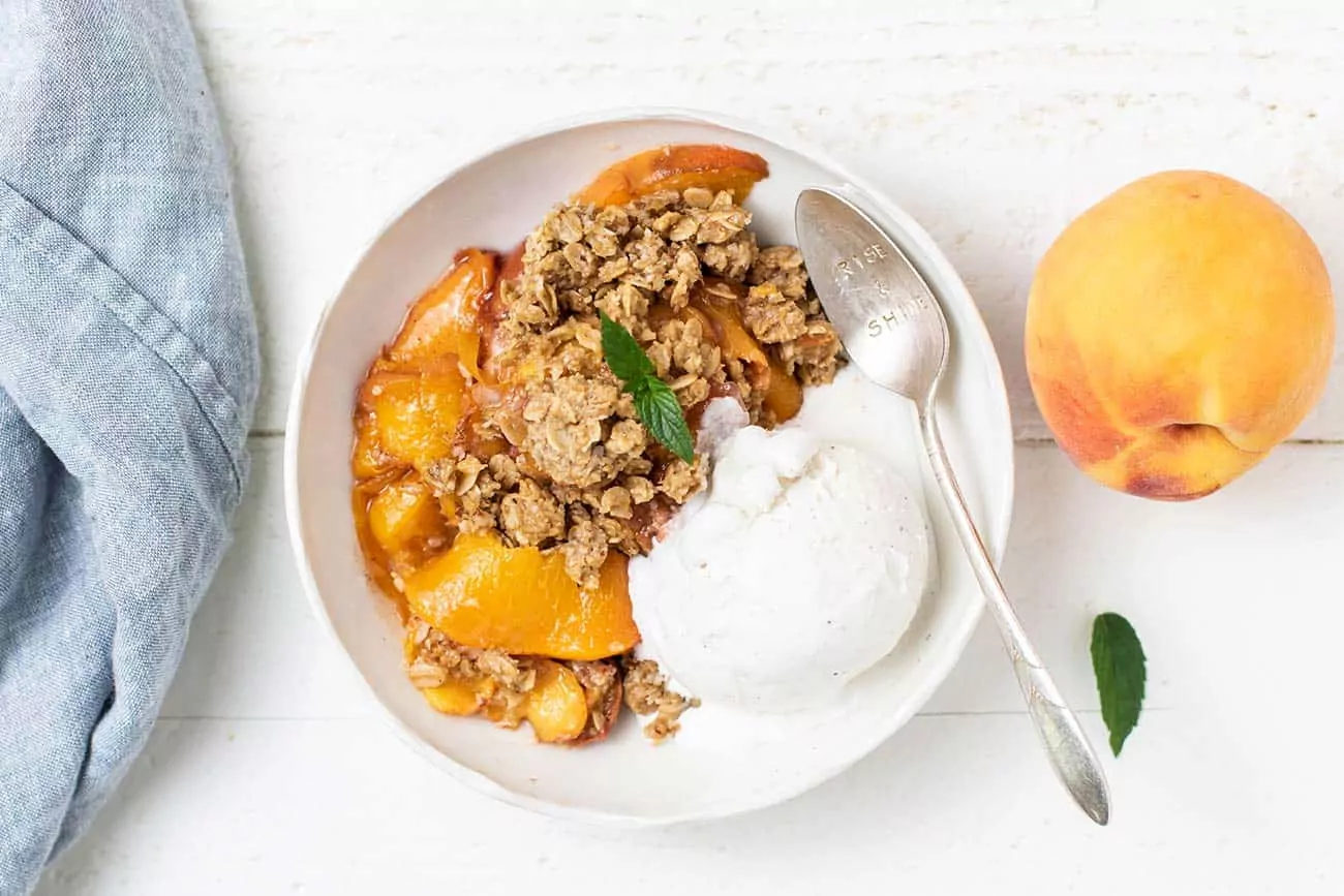 peach crisp with ice cream in bowl with spoon.