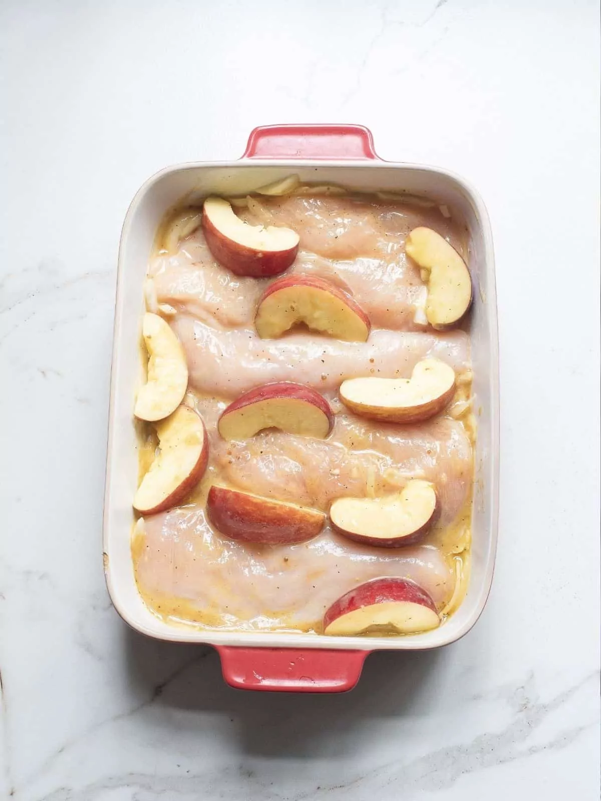 raw chicken and apples in baking dish.