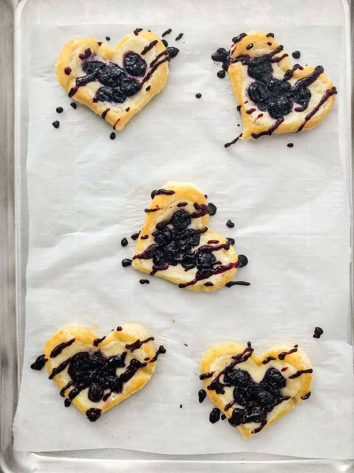 Baked puff pastry danish with blueberries on parchment paper lined tray.