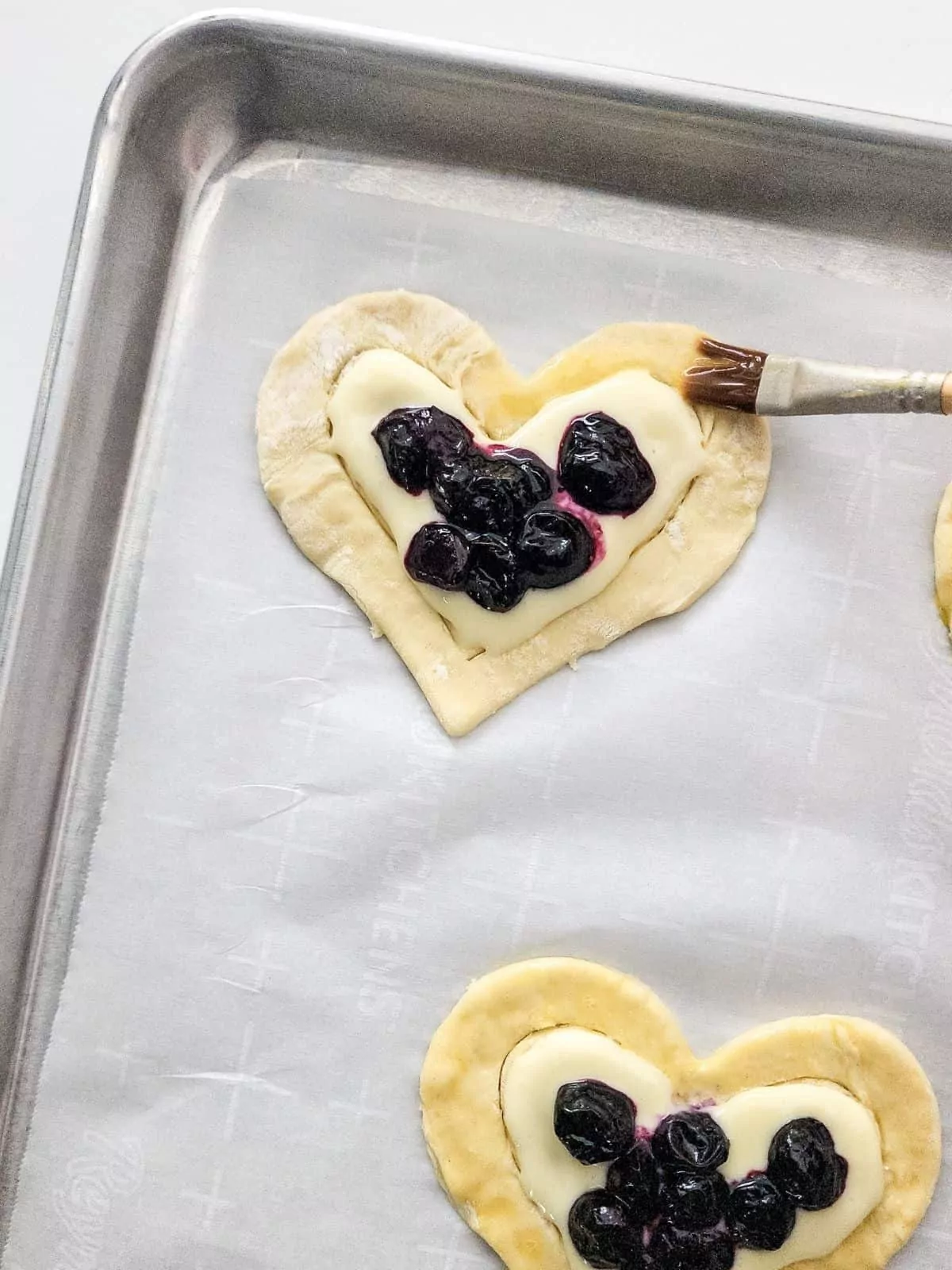 Brushing egg wash on puff pastry danish in shape of hearts.