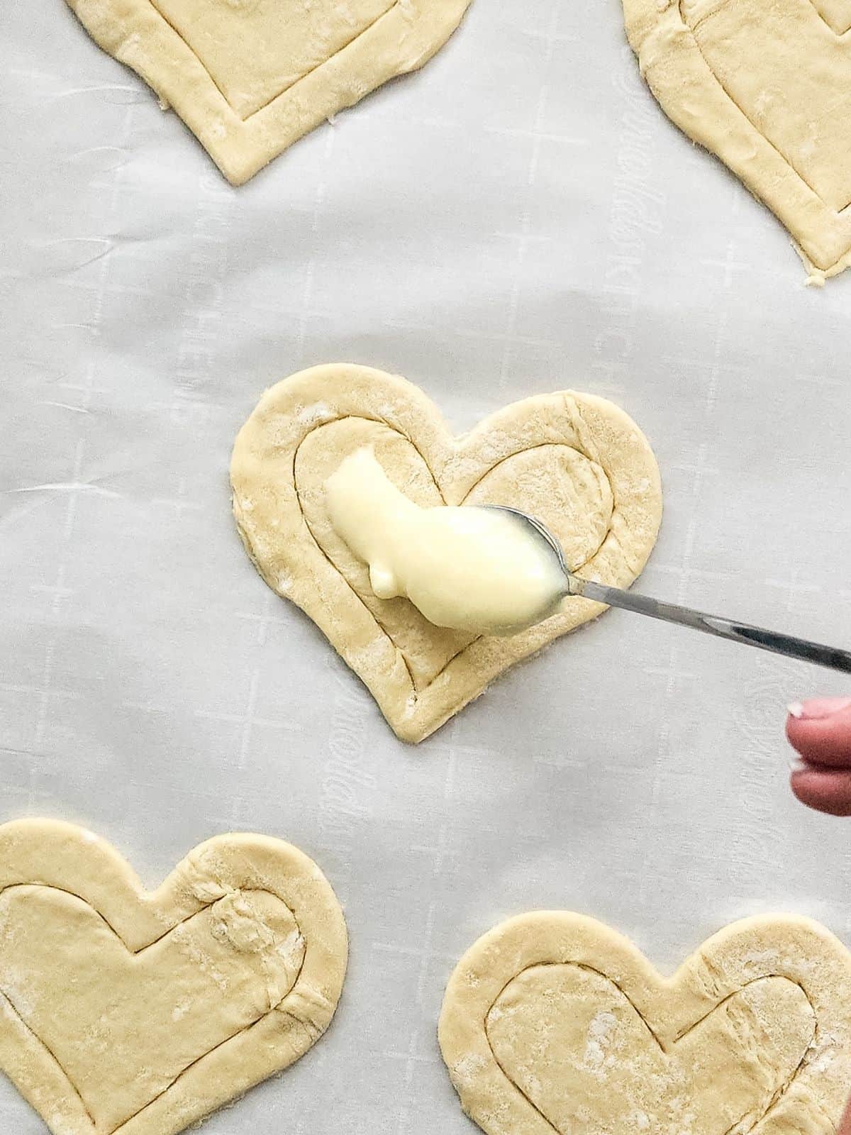Add cream cheese filling to center of puff pastry heart shapes.