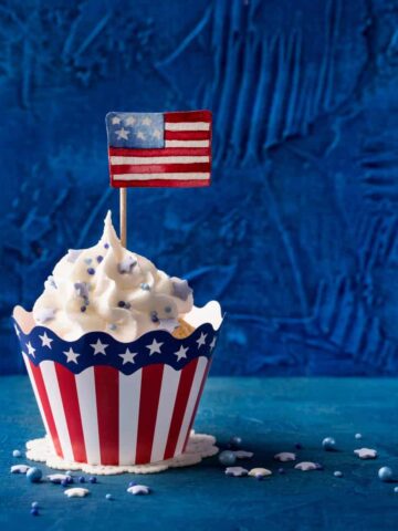 vanilla cupcake with frosting and blue sprinkles. Small American flag in the center of the cupcake.