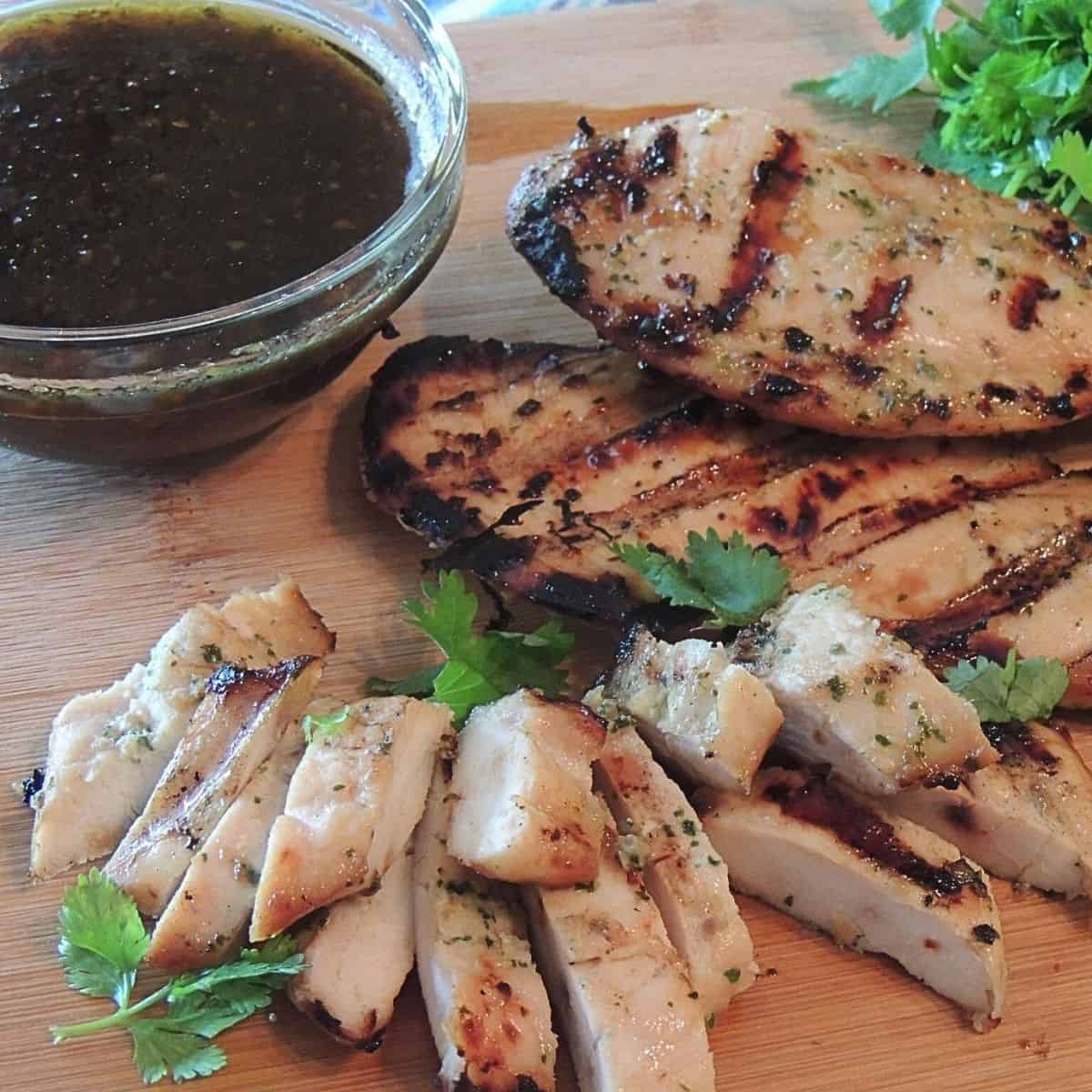 sliced grilled and whole chicken breast on cutting board.