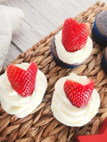 Red White and Blue Cupcakes. Plain blue cupcakes on the right - ones with white frosting and red strawberries on the left.