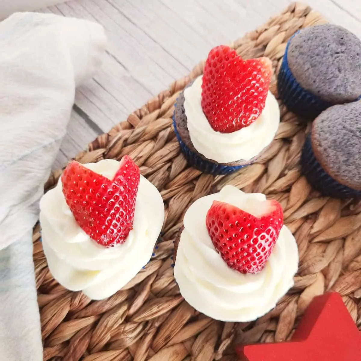 Red White and Blue Cupcakes. Plain blue cupcakes on the right - ones with white frosting and red strawberries on the left.