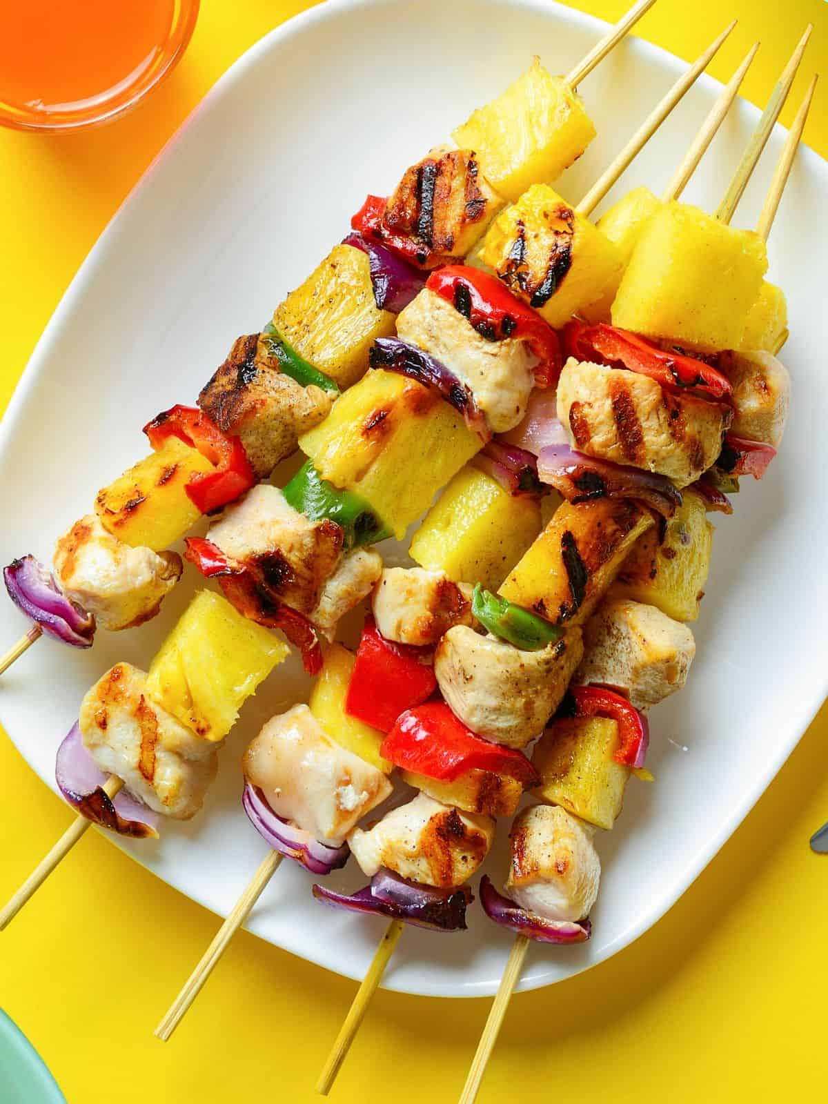 Chicken skewers on white plate with pineapple chunks.