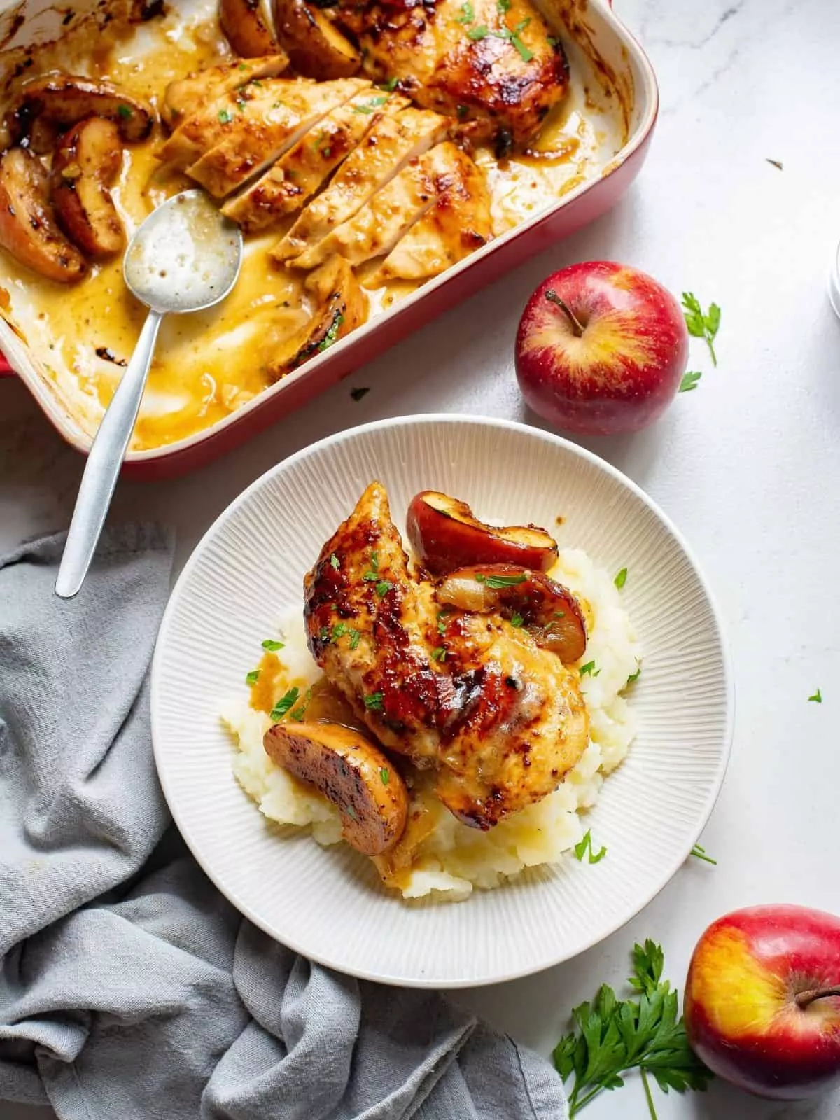 baked chicken with apples served over mashed potatoes on white plate.