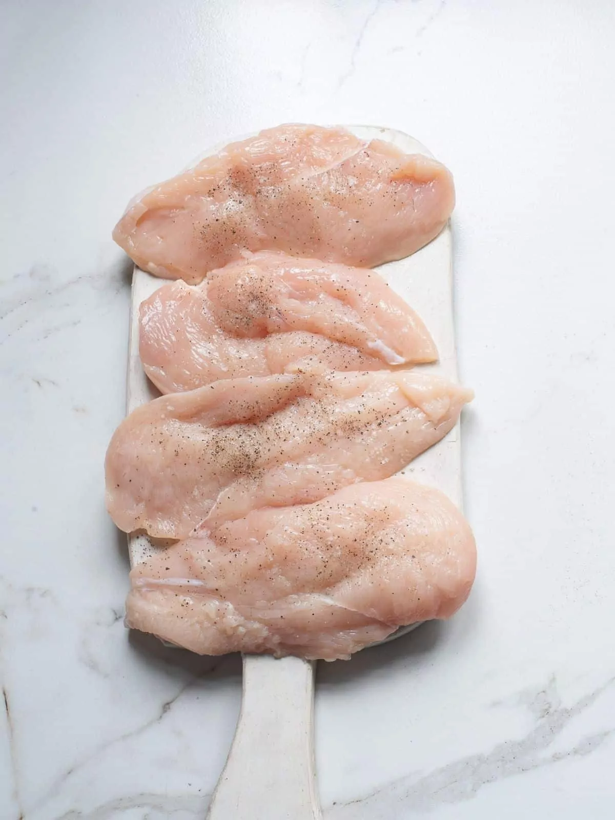 raw chicken breasts on cuttng board with salt and pepper.
