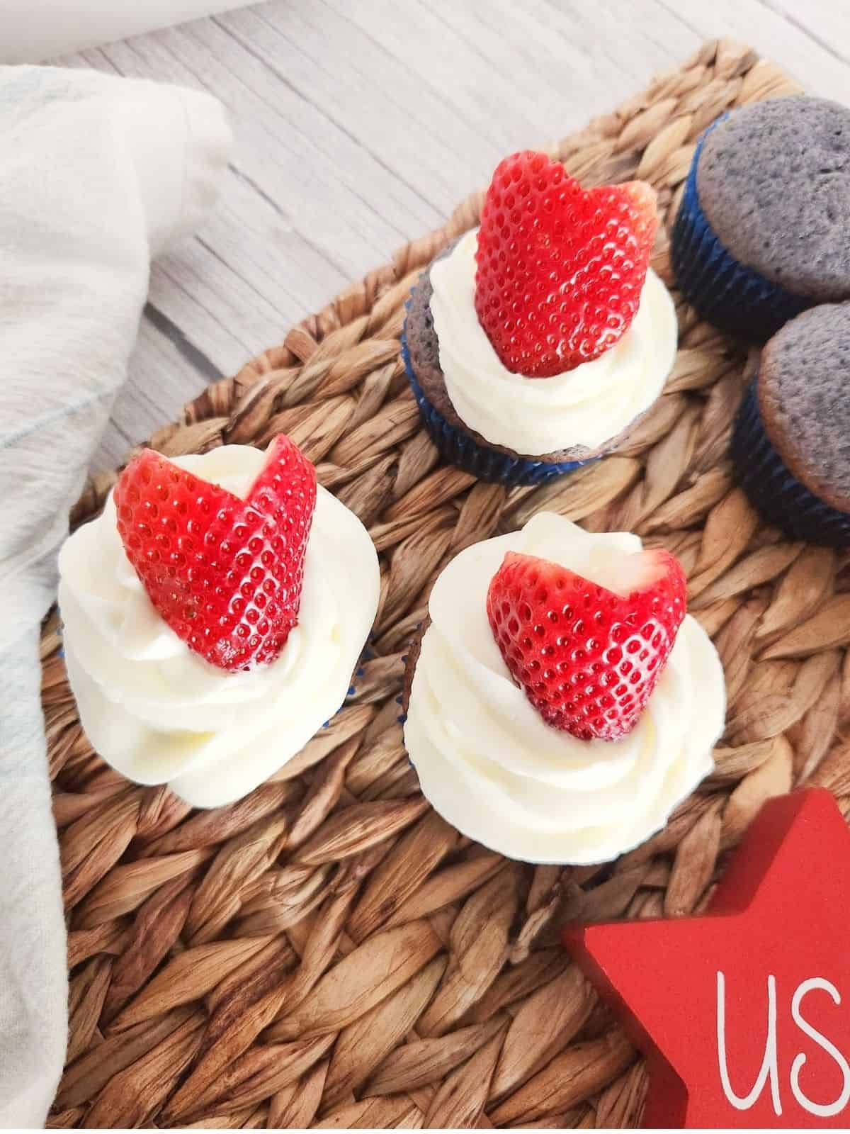 frosted blueberry cupcakes with strawberries on top.