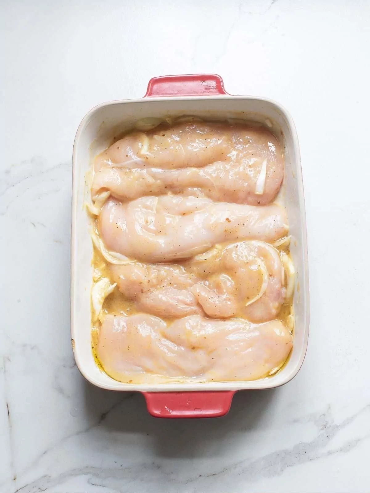 chicken breasts in casserole dish with marinade and onions.