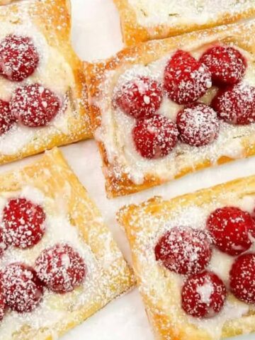 Six raspberry tarts on a white plate.