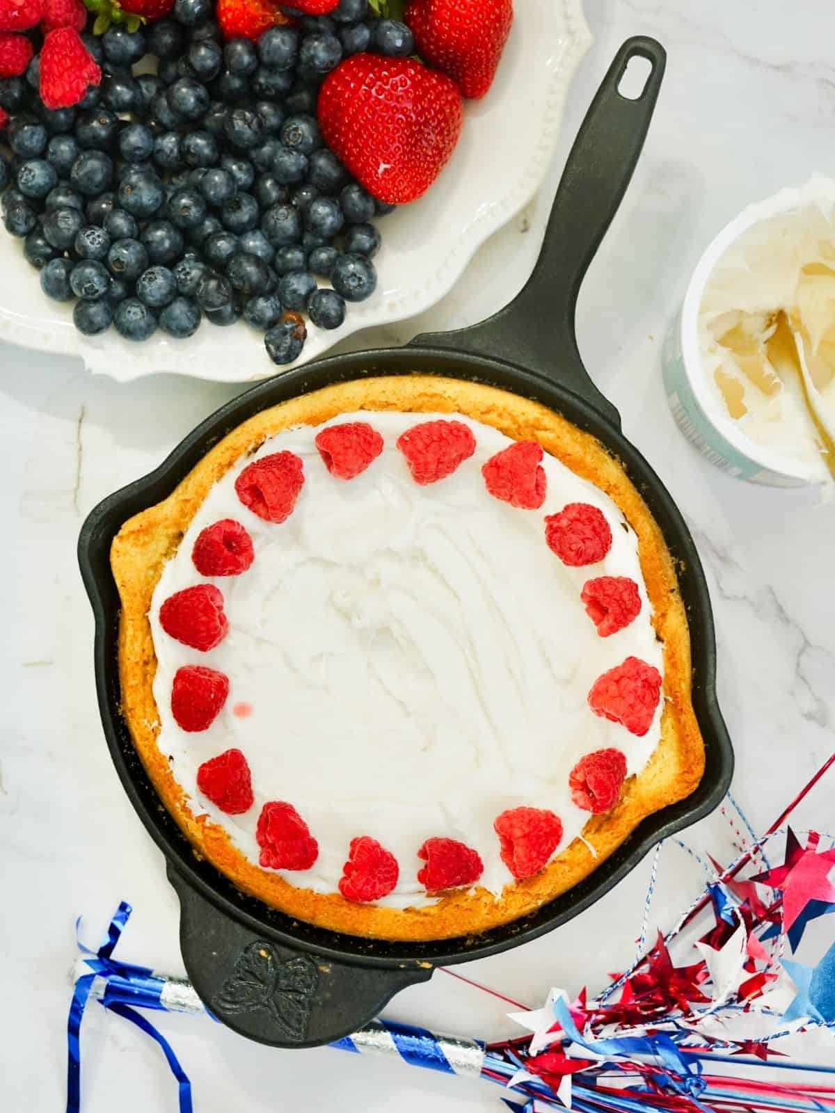 skillet sugar cookie cake with cream cheese frosting and fresh raspberries.