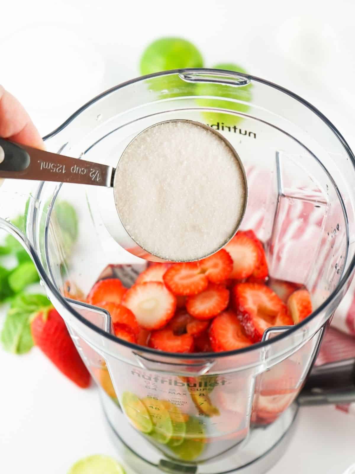 adding sugar to blender with strawberries.