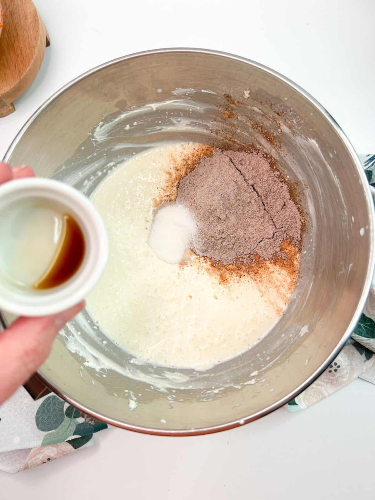 vanilla extract in small bowl being held over larger bowl with pudding ingredients.