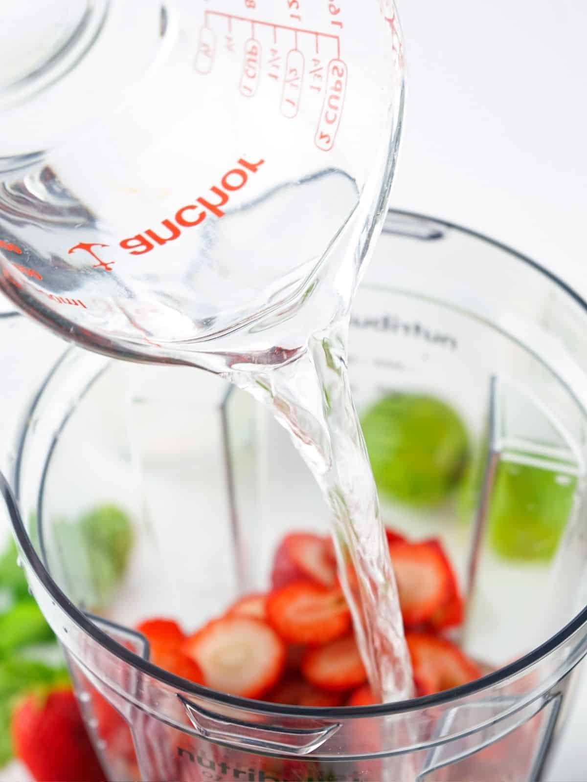 adding water and lime juice to blender with strawberries.