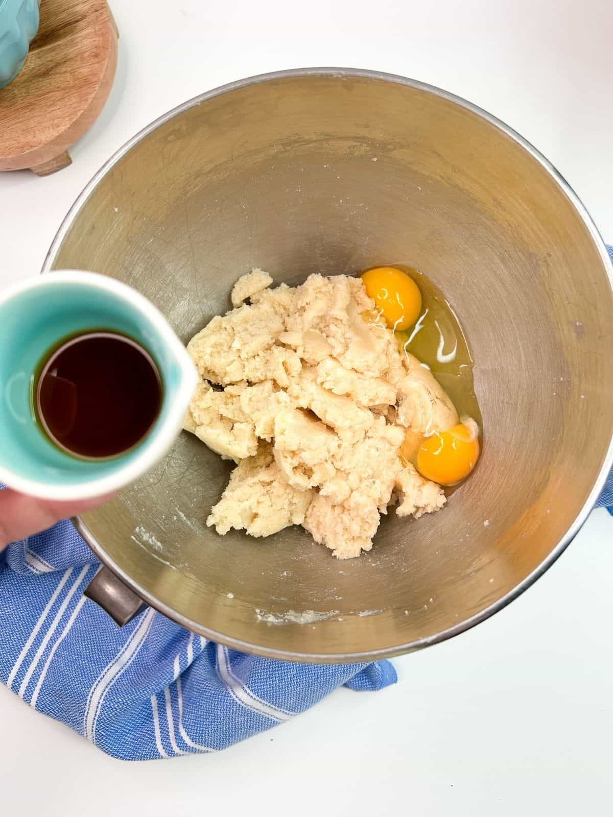adding vanilla extract to eggs, butter, sugar mixture in mixing bowl.