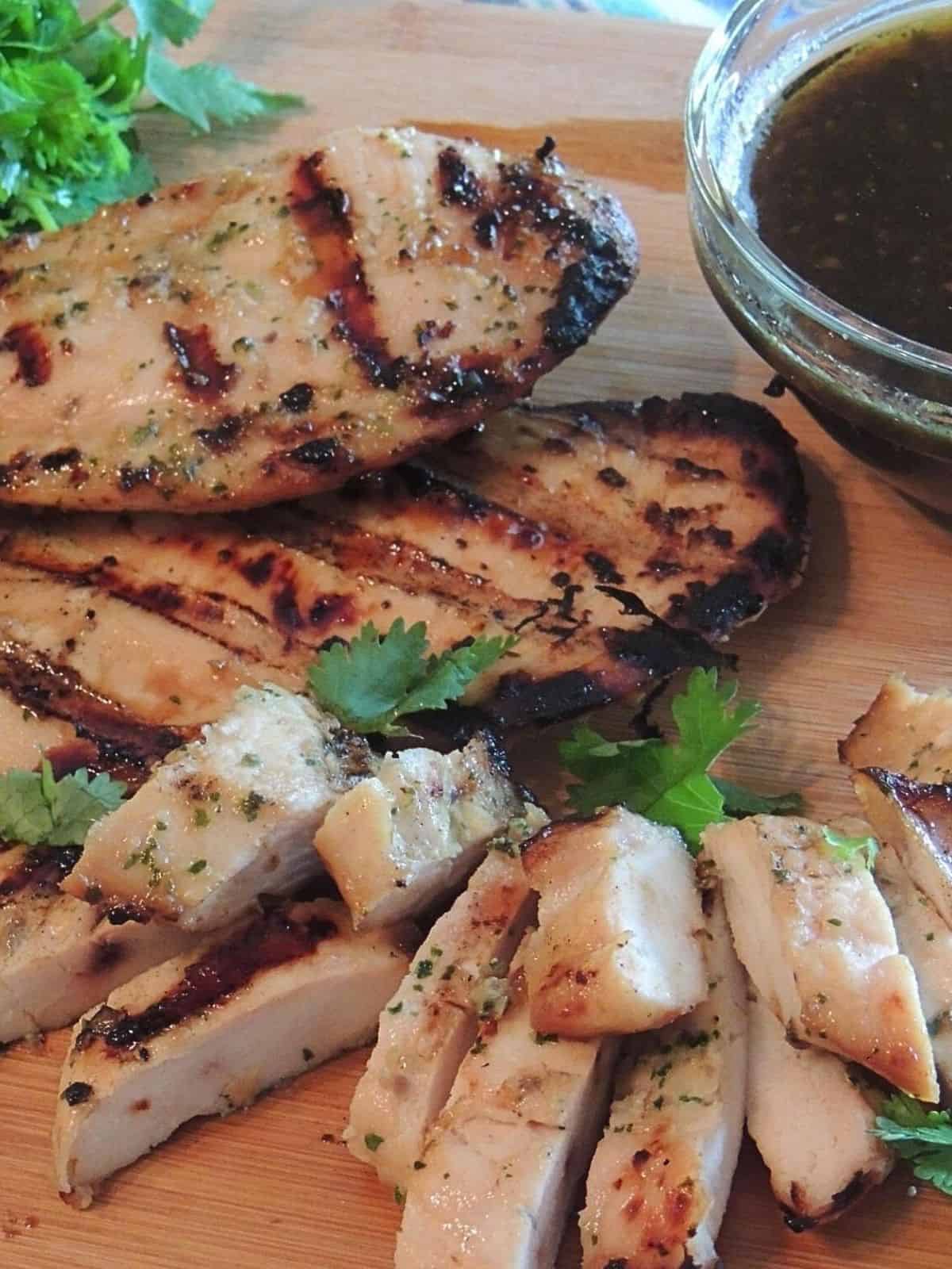 Grilled chicken breasts and sliced on cutting board.