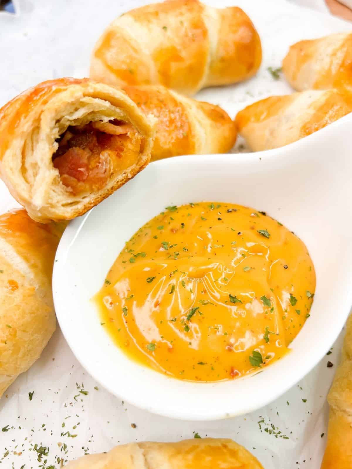 closeup of bacon inside crescent roll over bowl of sauce.