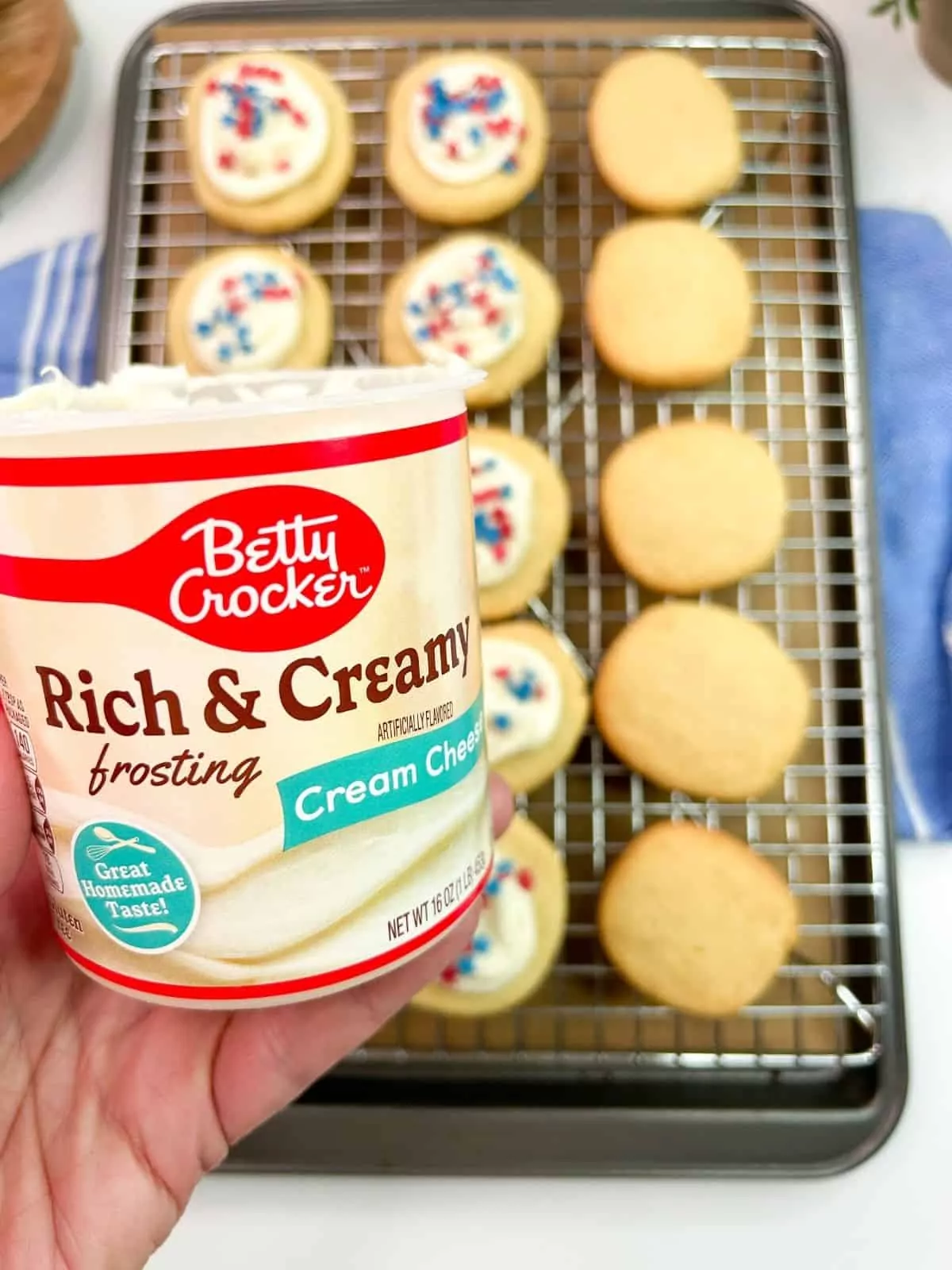 Canned cream cheese frosting being held over tray of baked cookies.