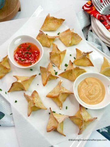 won tons baked on white platter with two different dipping sauces.