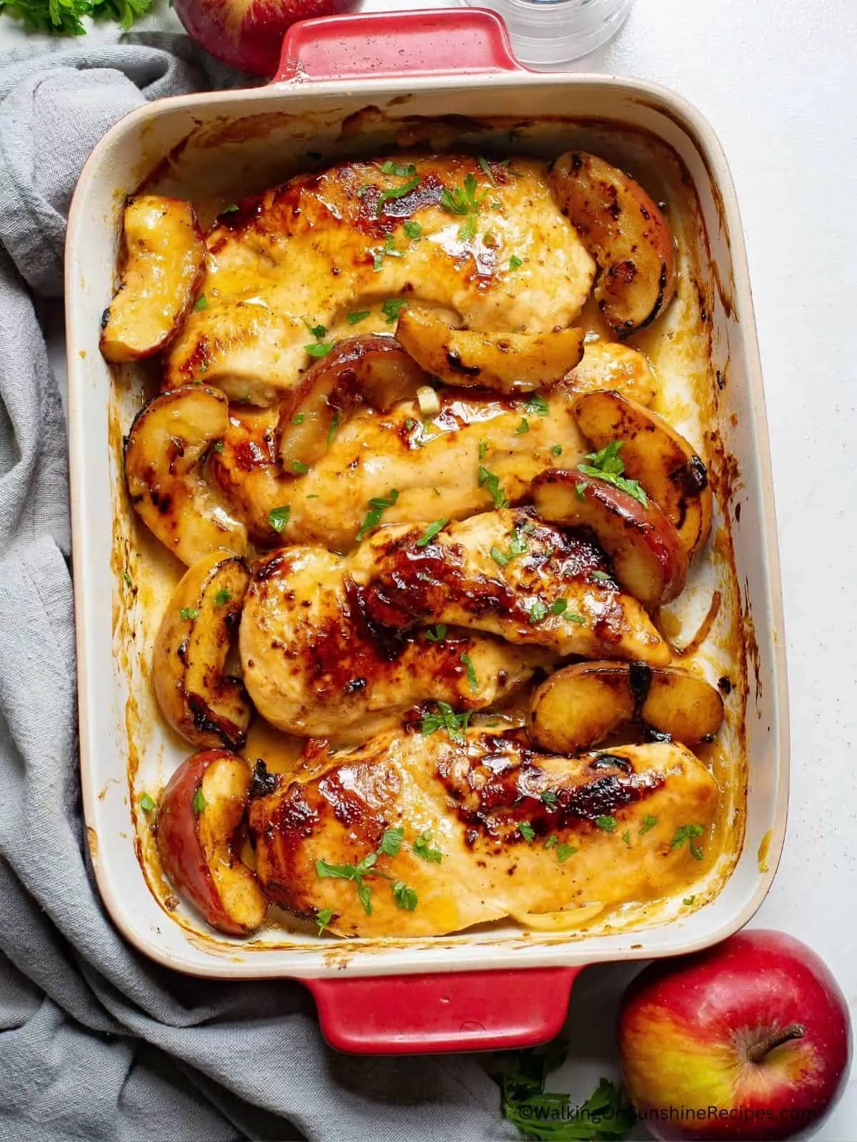 baked chicken breasts with apples in casserole dish with whole apple on side.