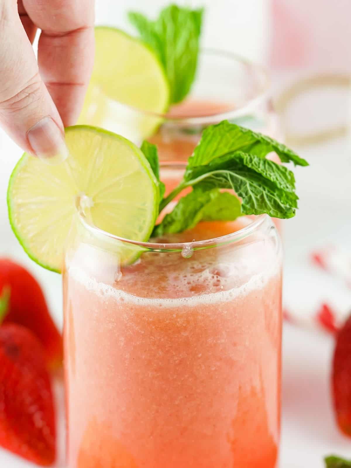 Adding lime slice to glass of strawberry water.