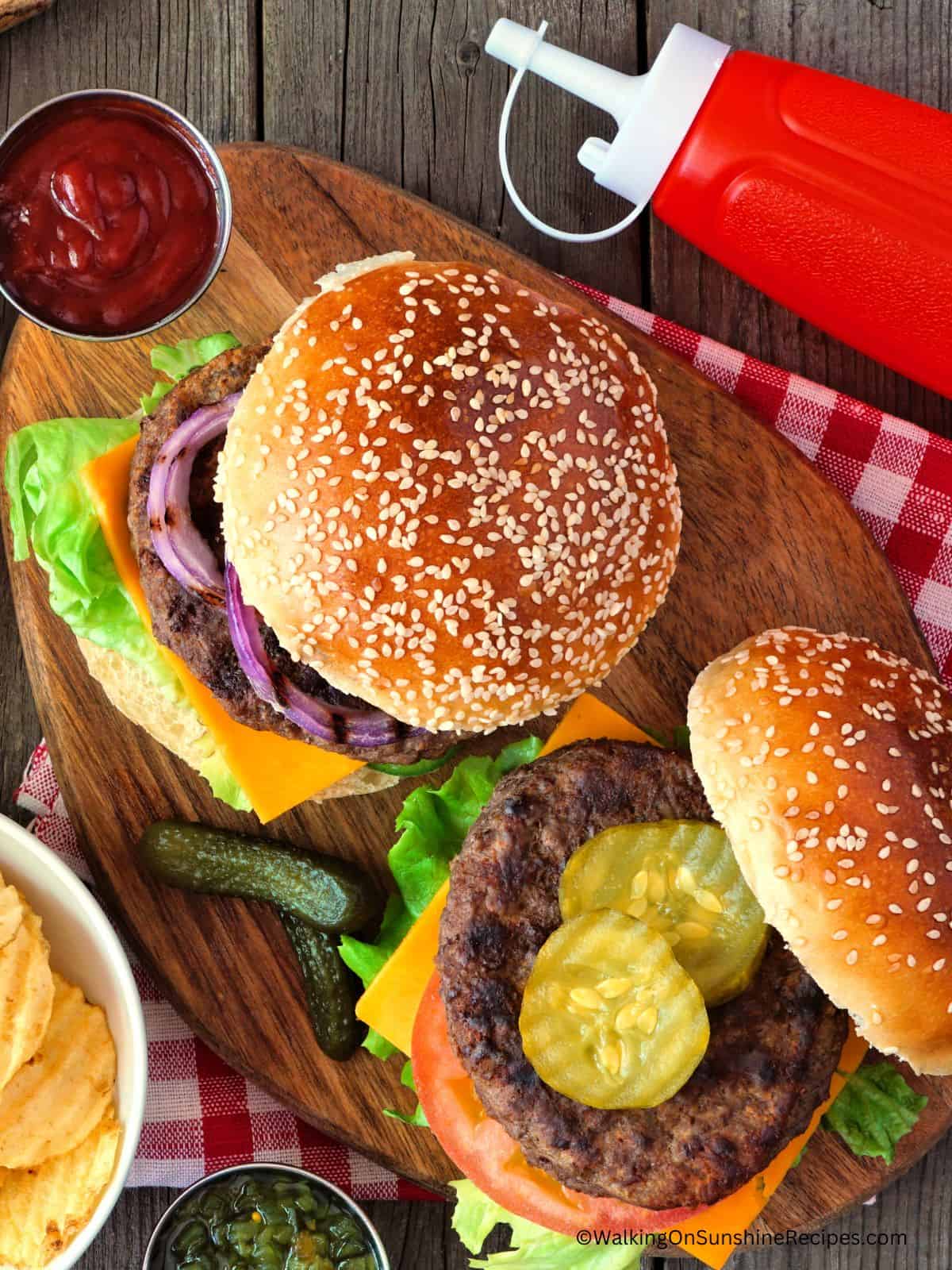 hamburgers with toppings on cutting board and red checked napkin.
