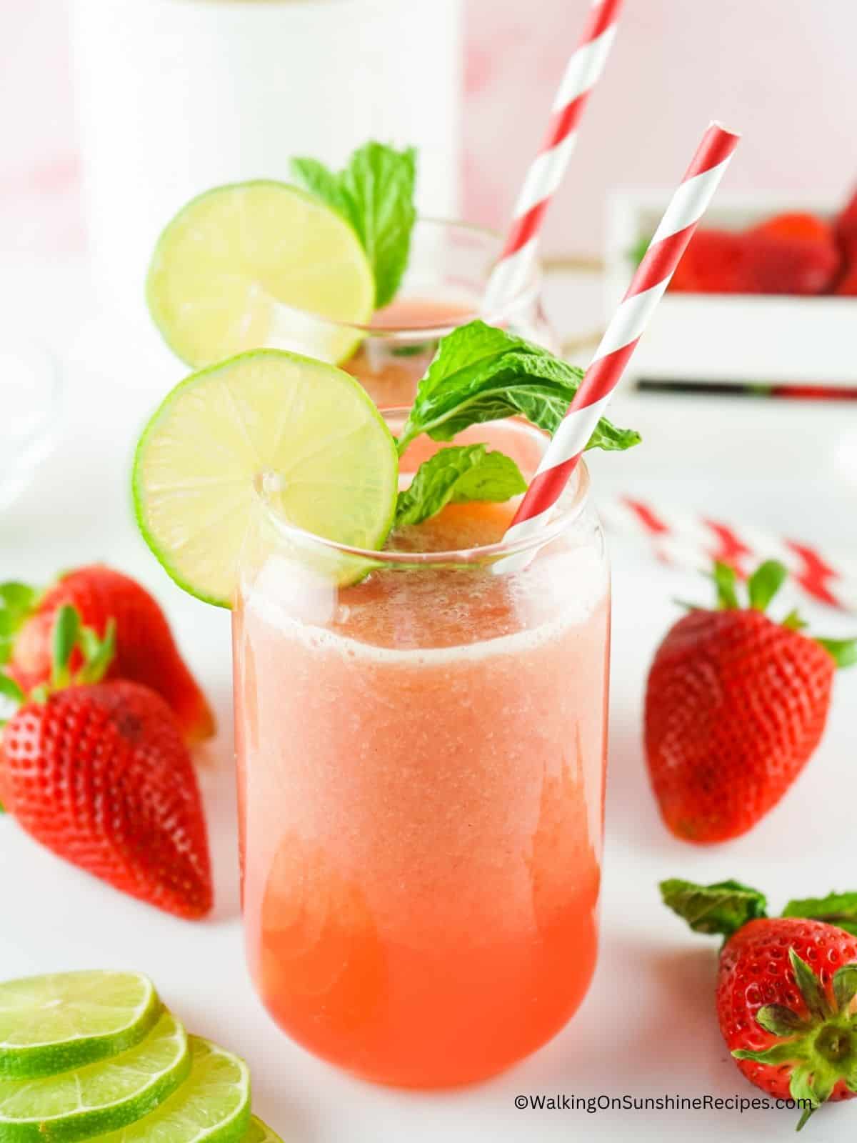 2 glasses of strawberry lime beverage with straws and fresh lime slices as garnish.