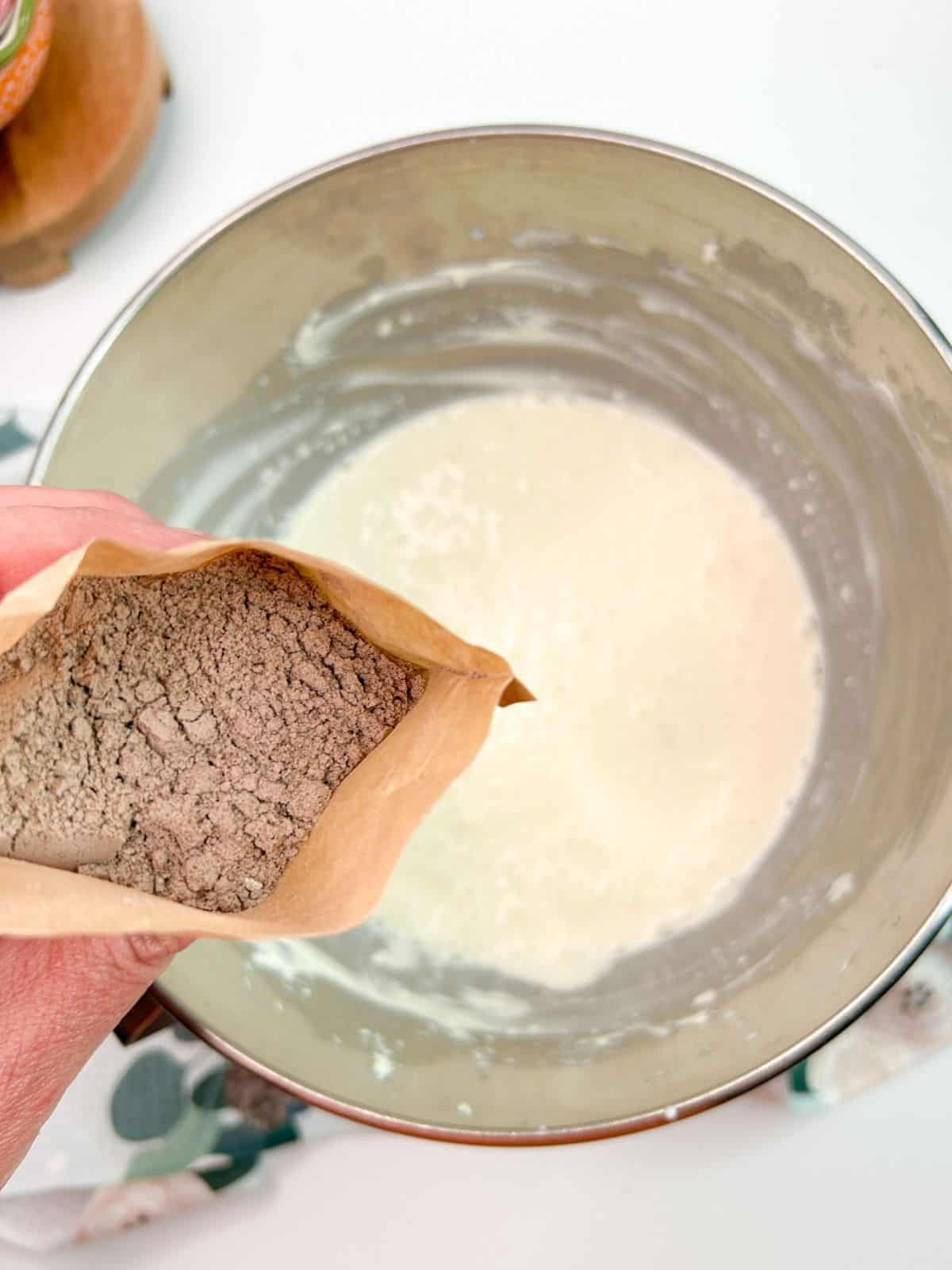Pudding mix being held over mixing bowl of cream cheese.