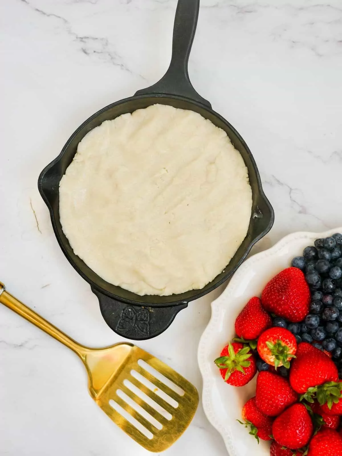 sugar cookie dough in cast iron skillet with fruit in plate.