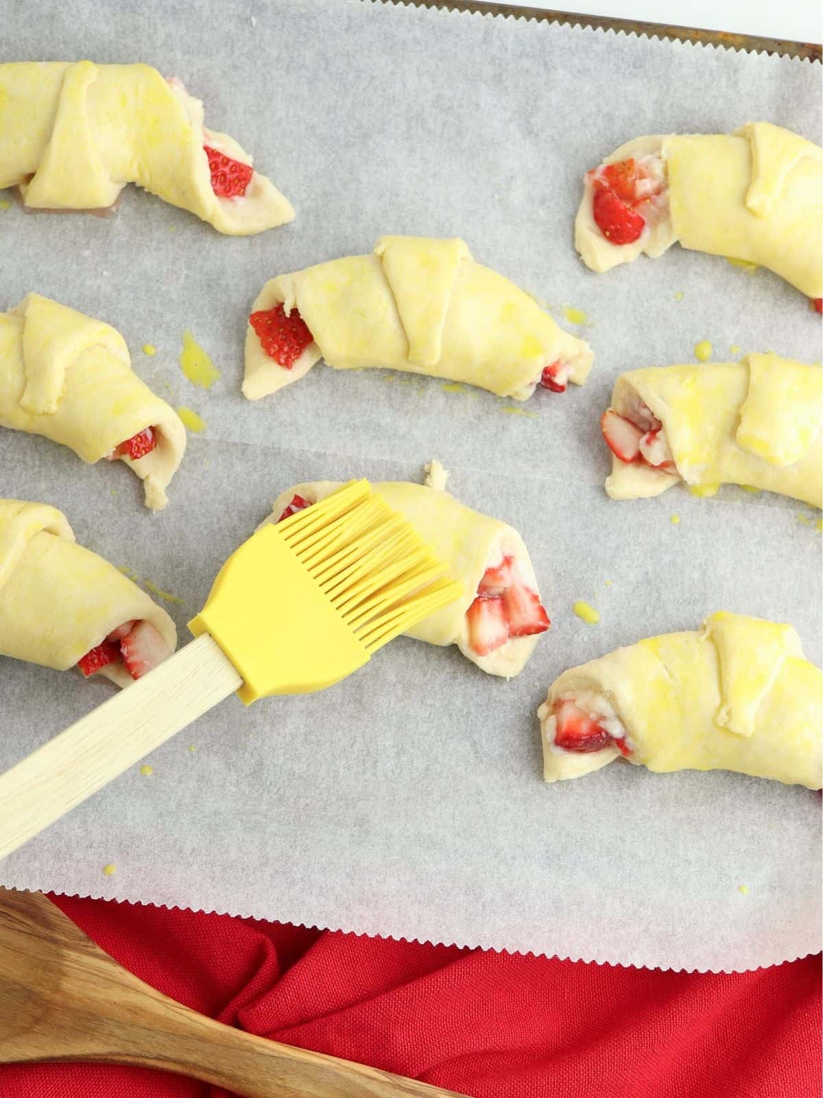 Raw crescent rolls with strawberries on baking tray.