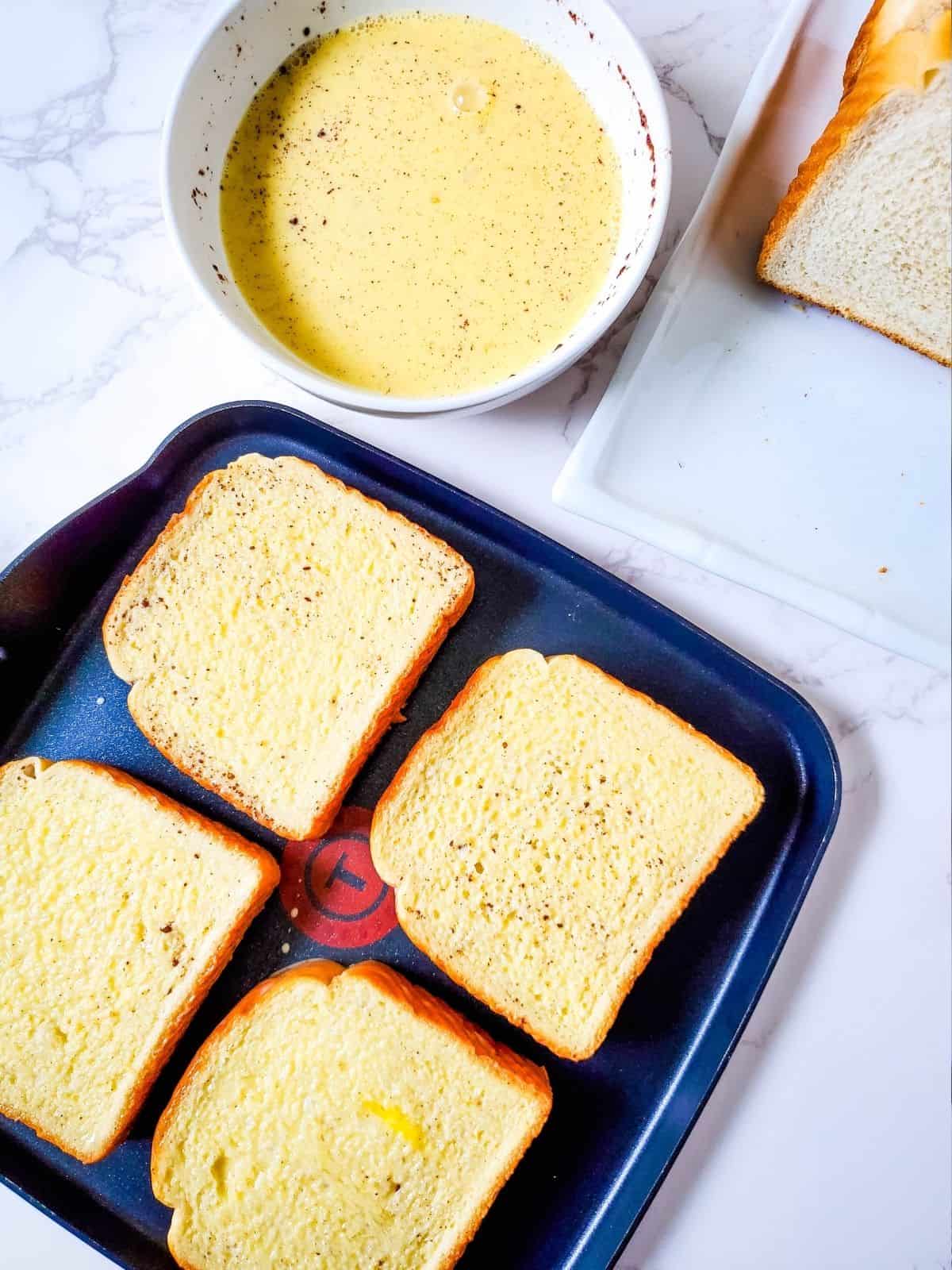 Egg dipped bread slices on frying pan.