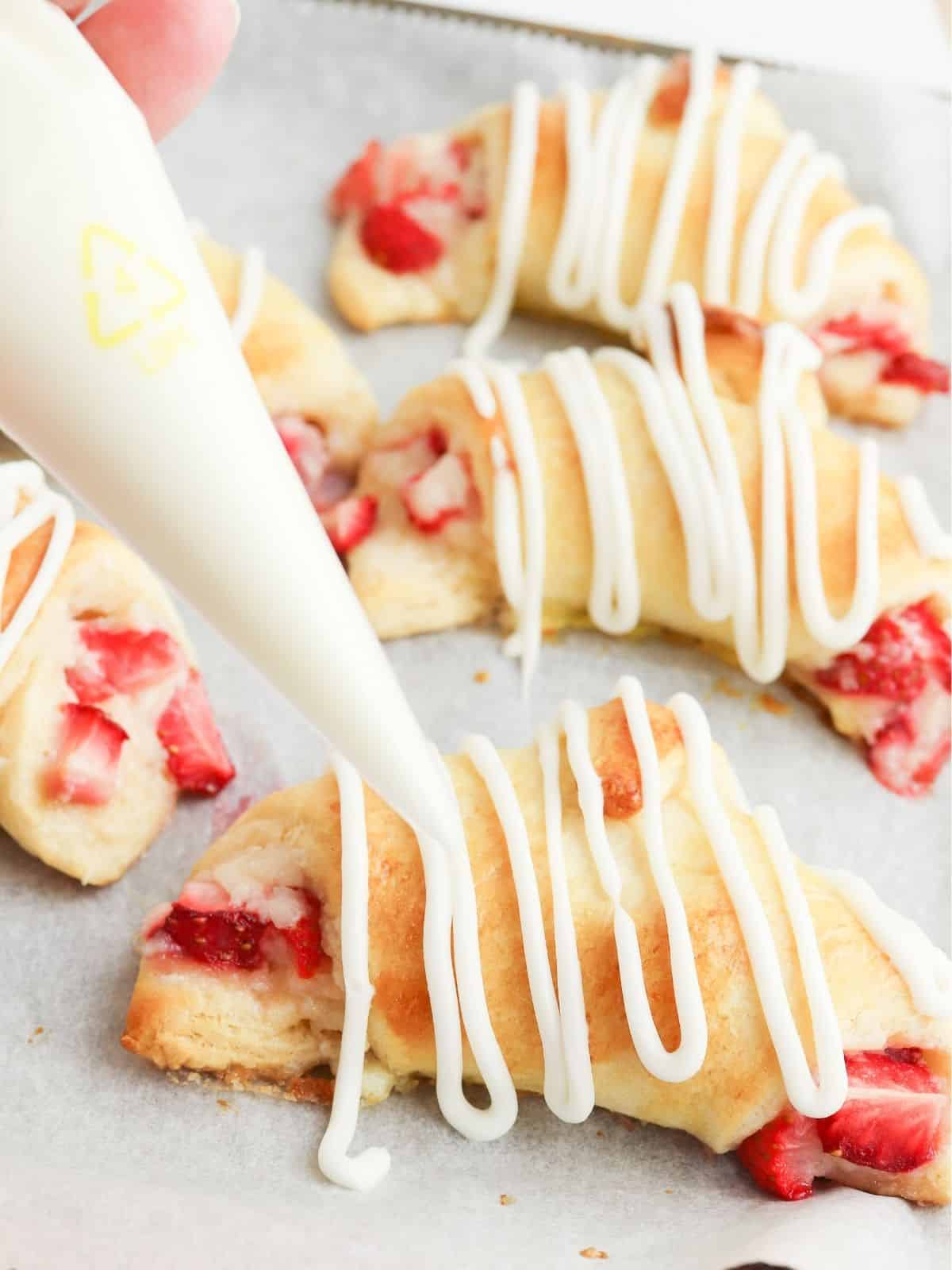 Drizzle powdered sugar glaze on top of crescent rolls filled with strawberries.