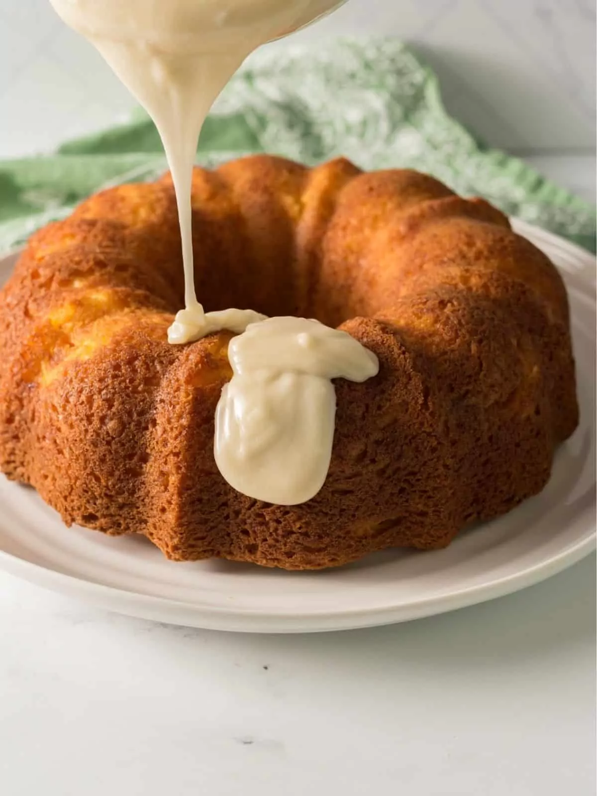 Pouring cream cheese frosting on top of peach bundt cake.