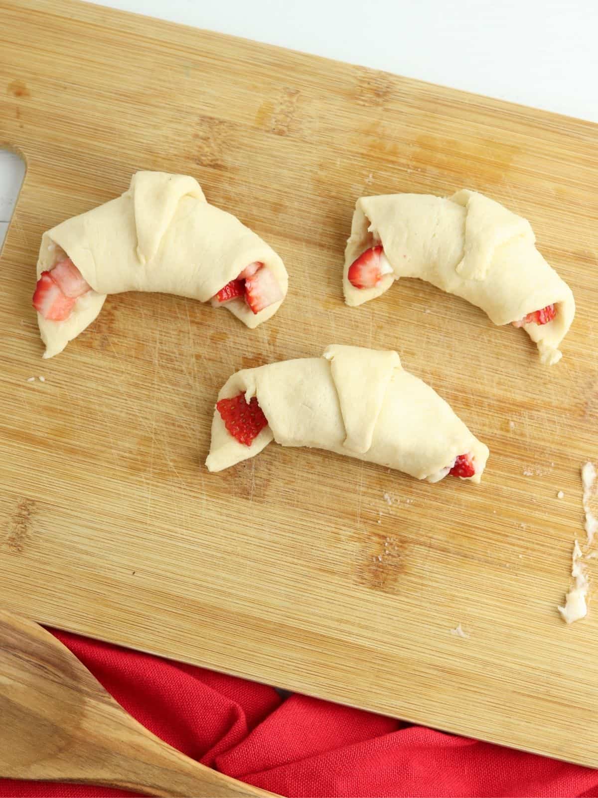 crescent rolls filled with strawberries on cutting board.
